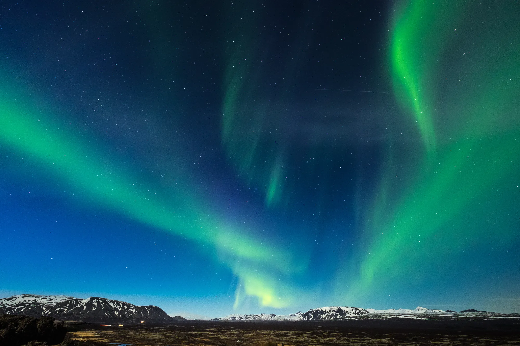 Green aurora curtains over snow-covered mountains in Iceland on a clear, dark night