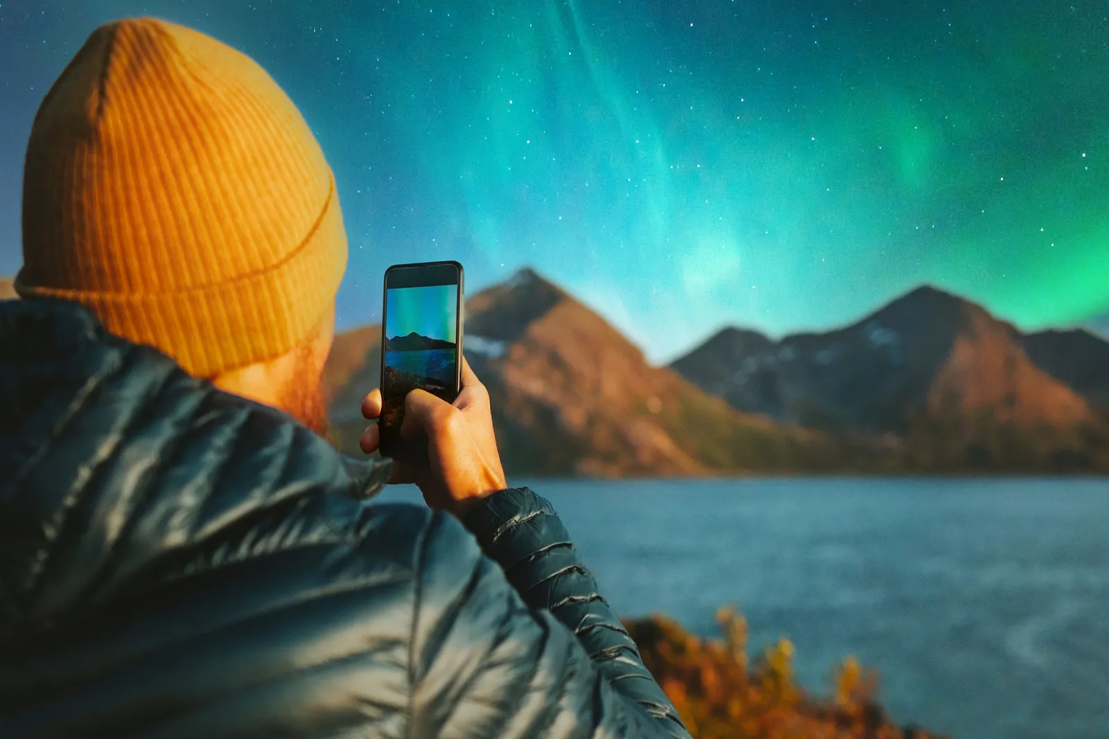 Checking the aurora on a phone while the sky performs — northern-lights hunting in the far north is a phone-in-hand sport